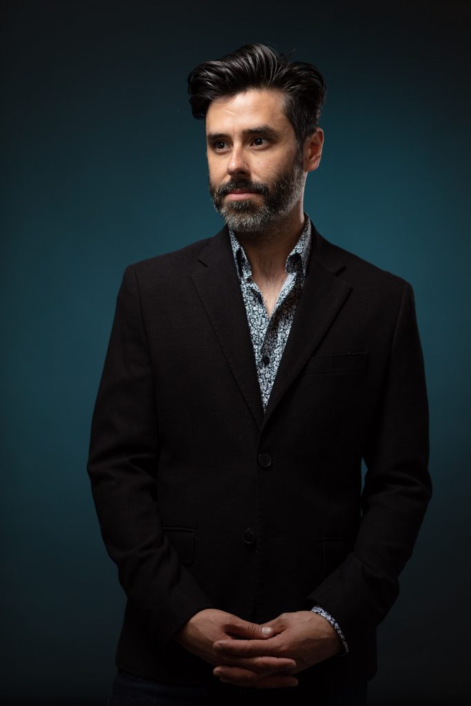 Portrait of a bearded middle age while man wearing a suit jacket on a blue background by corporate portrait photographer Nick Reid.